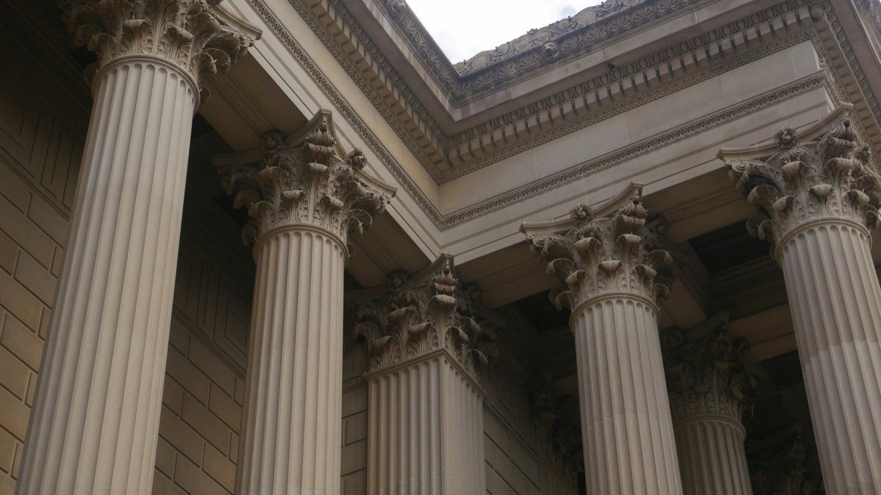 Fluted classical columns with carved capitals beneath a stone cornice, seen from below