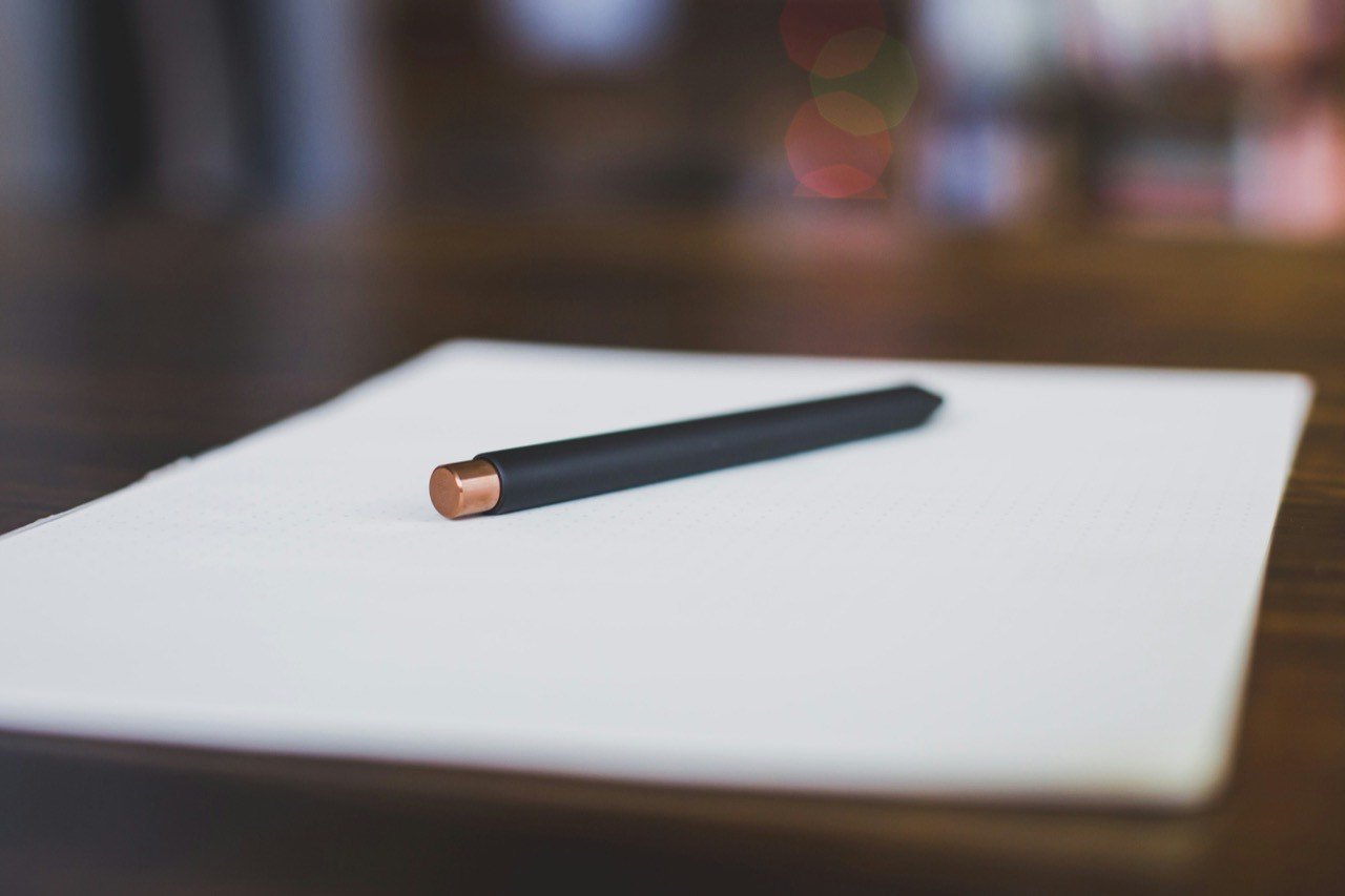 A black pen lying on a white dotted notepad on a wooden desk
